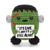A handmade crochet animal doll with green body and gray ears, featuring a card that reads It's live and it's still alive.