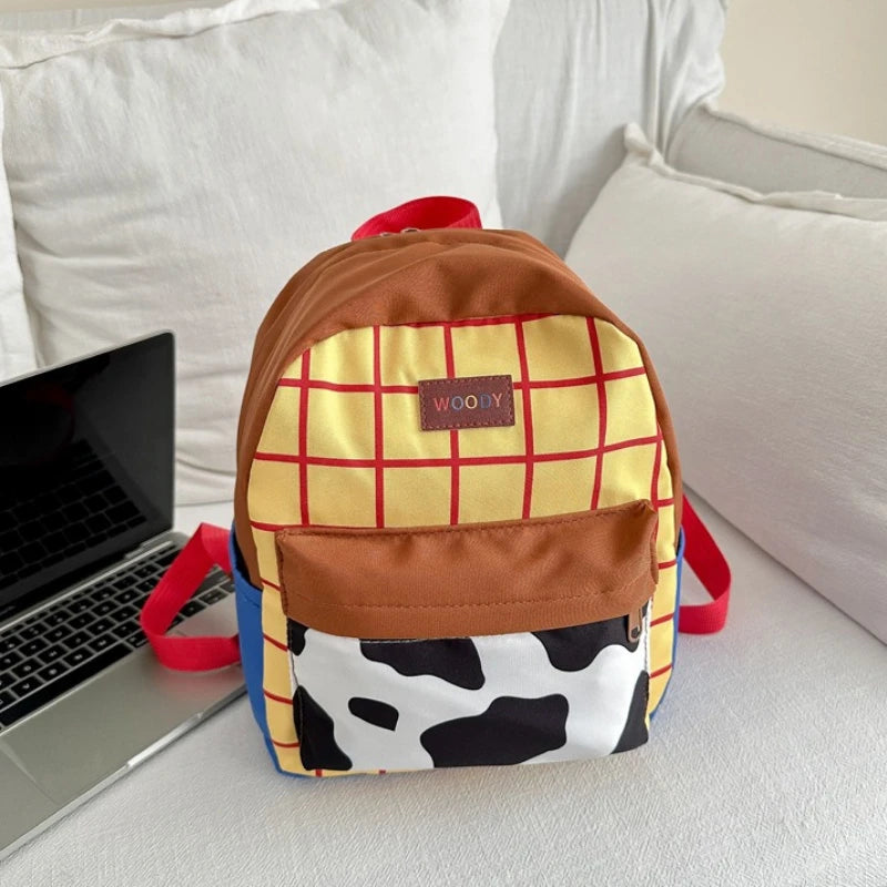 A brown and yellow plaid backpack with a cow print front is resting on a white surface next to a silver laptop.