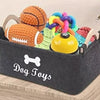 A gray felt storage basket filled with various colorful dog toys including a ball and a ring.