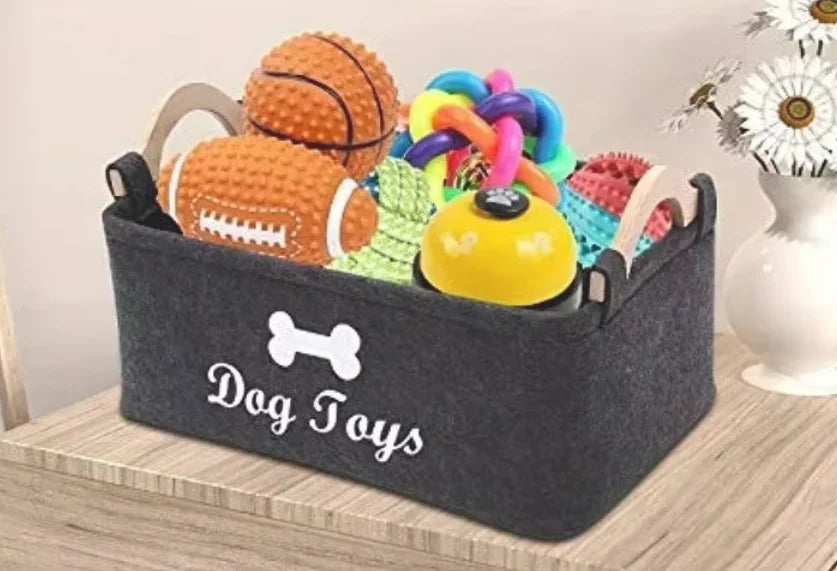 A gray felt storage basket filled with various colorful dog toys including a ball and a ring.