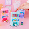 A pink interactive vending machine toy with slots for play coins and drinks is held by a hand against a pink background.