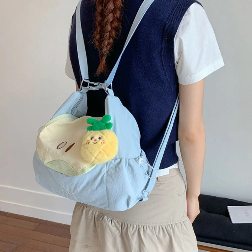 A person is wearing a light blue nylon messenger bag decorated with a yellow lemon charm and a dark blue vest.