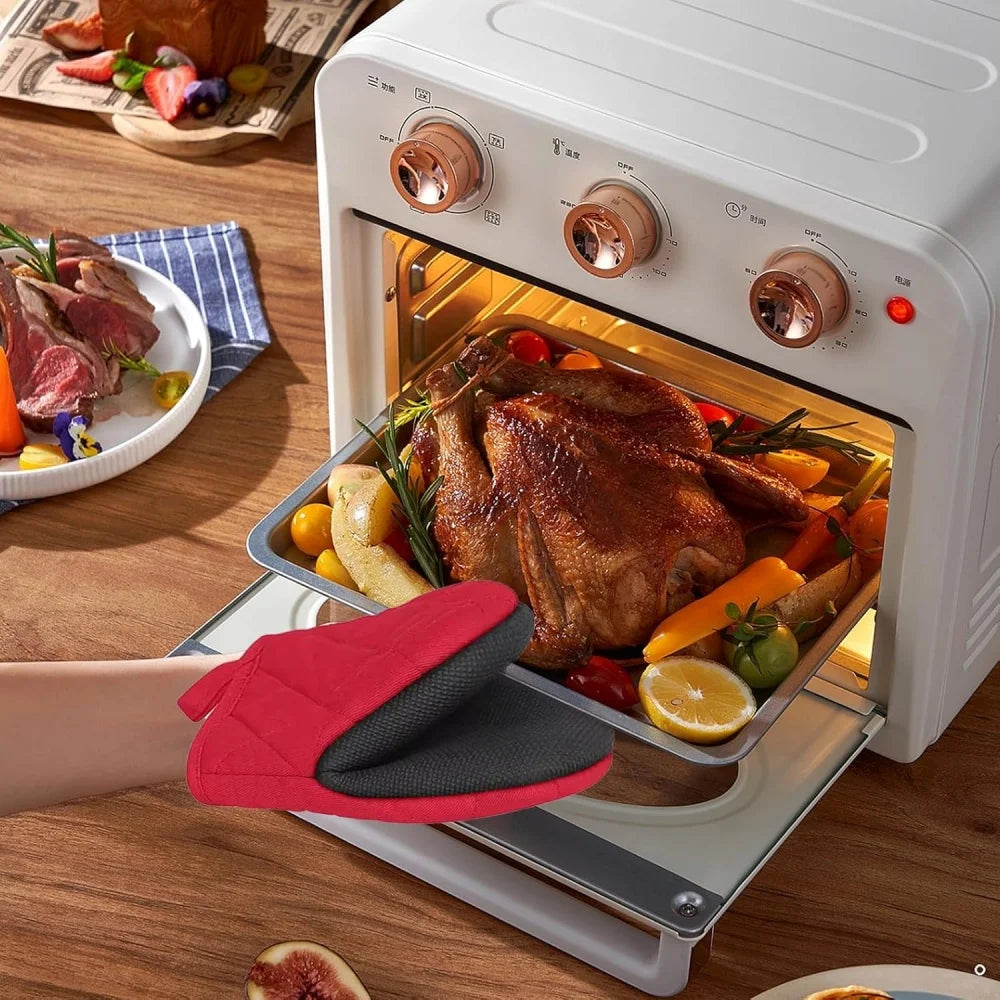 A pair of red and black heat-resistant silicone oven mitts are shown resting on a baking tray inside an open electric oven.