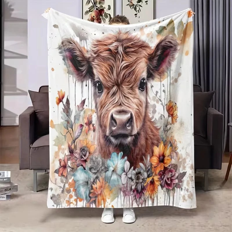 A flannel blanket featuring a painting of a brown Highland cow surrounded by colorful floral elements.