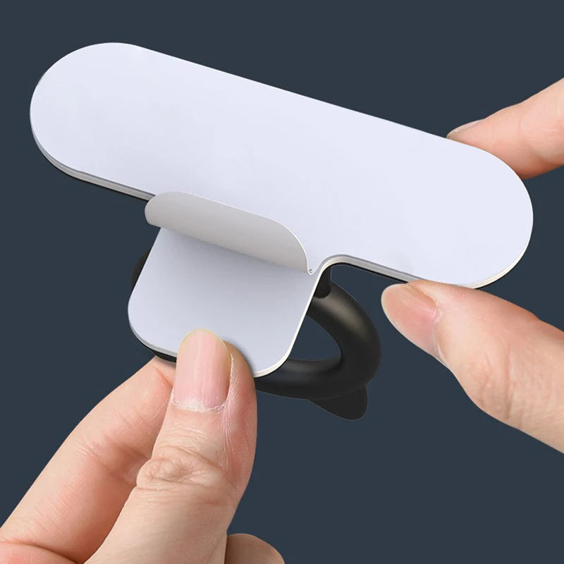 A hand is lifting a white silicone toilet lid lifter with a self-adhesive hook.