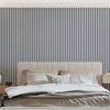 A bedroom featuring a bed with white linens against a dark gray and white vertical striped wallpaper.