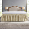 A beige elastic wrap-around bed skirt with ruffles covering a bed frame and headboard.