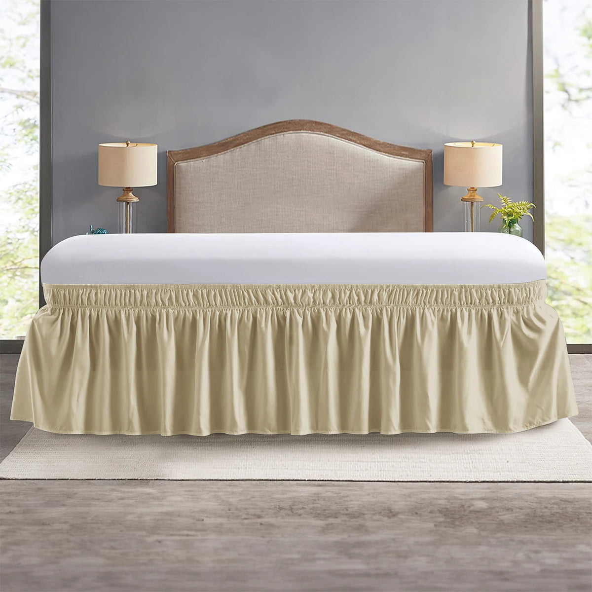 A beige elastic wrap-around bed skirt with ruffles covering a bed frame and headboard.