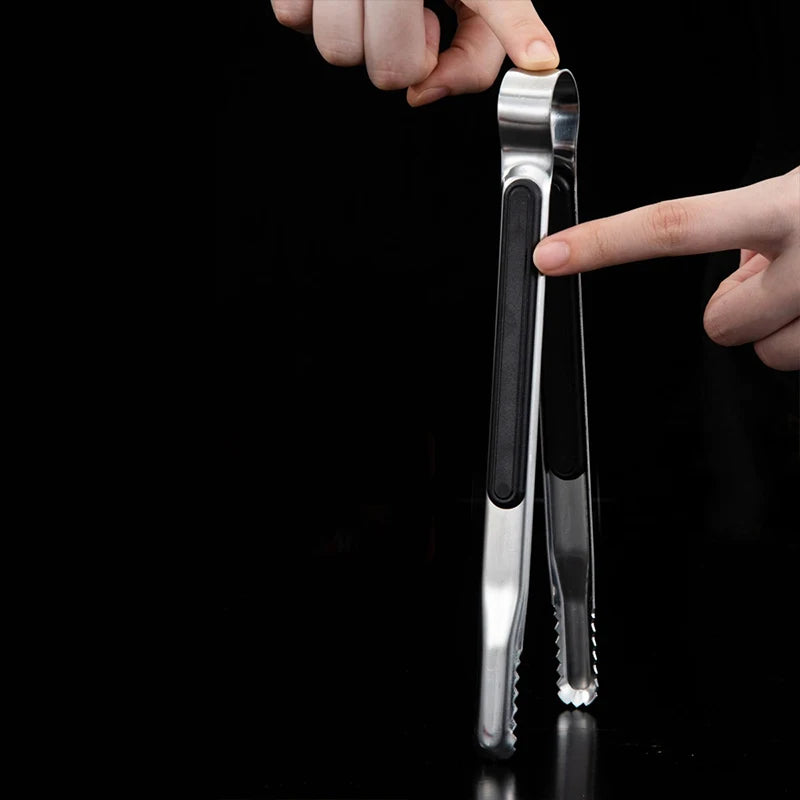 A hand is holding a premium stainless steel BBQ tongs against a black background.