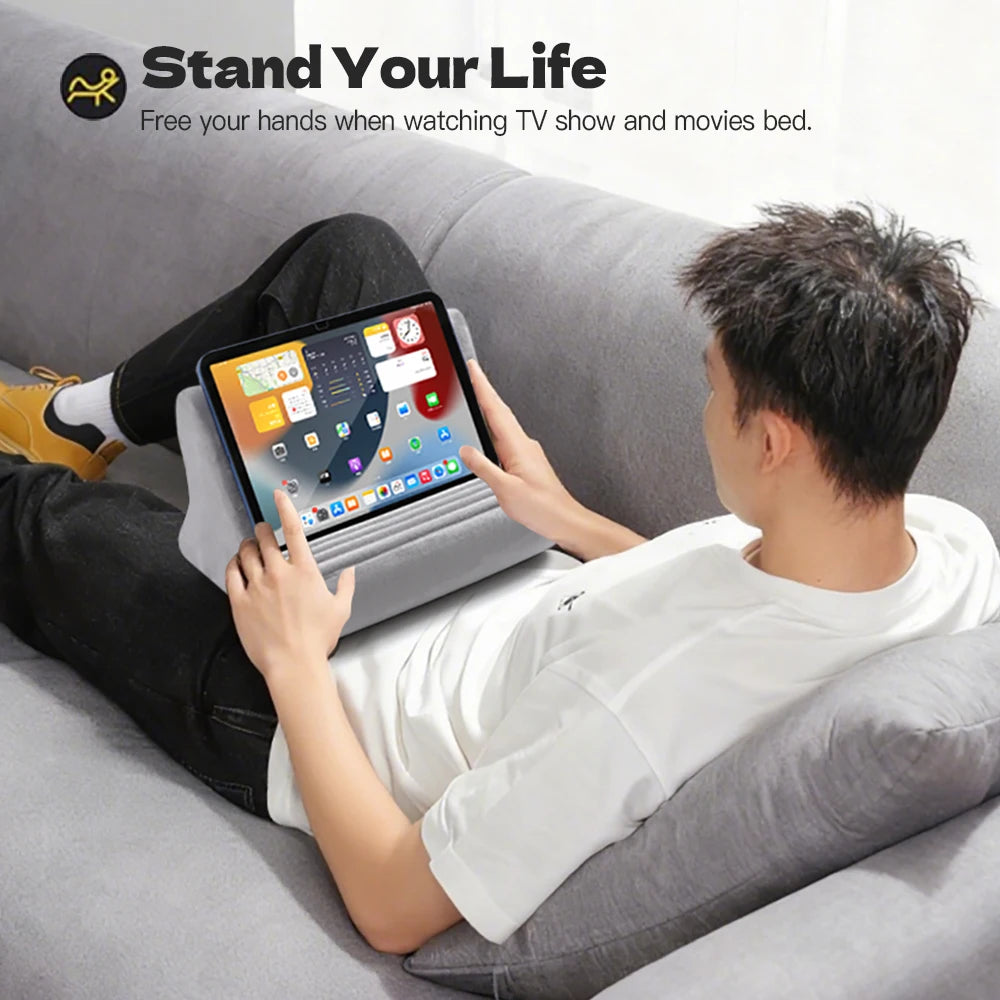 A person is using an adjustable comfort tablet and phone stand pillow while relaxing on a couch.