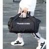 A black duffel bag with the brand name HONGYASE is being carried by a person wearing light-colored pants and white sneakers.