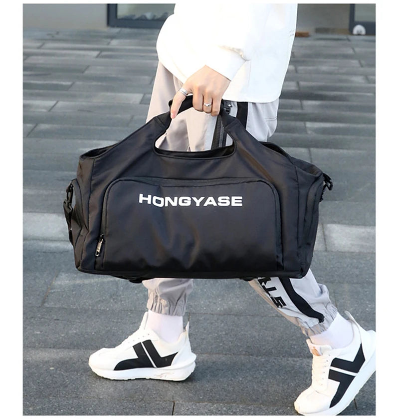A black duffel bag with the brand name HONGYASE is being carried by a person wearing light-colored pants and white sneakers.