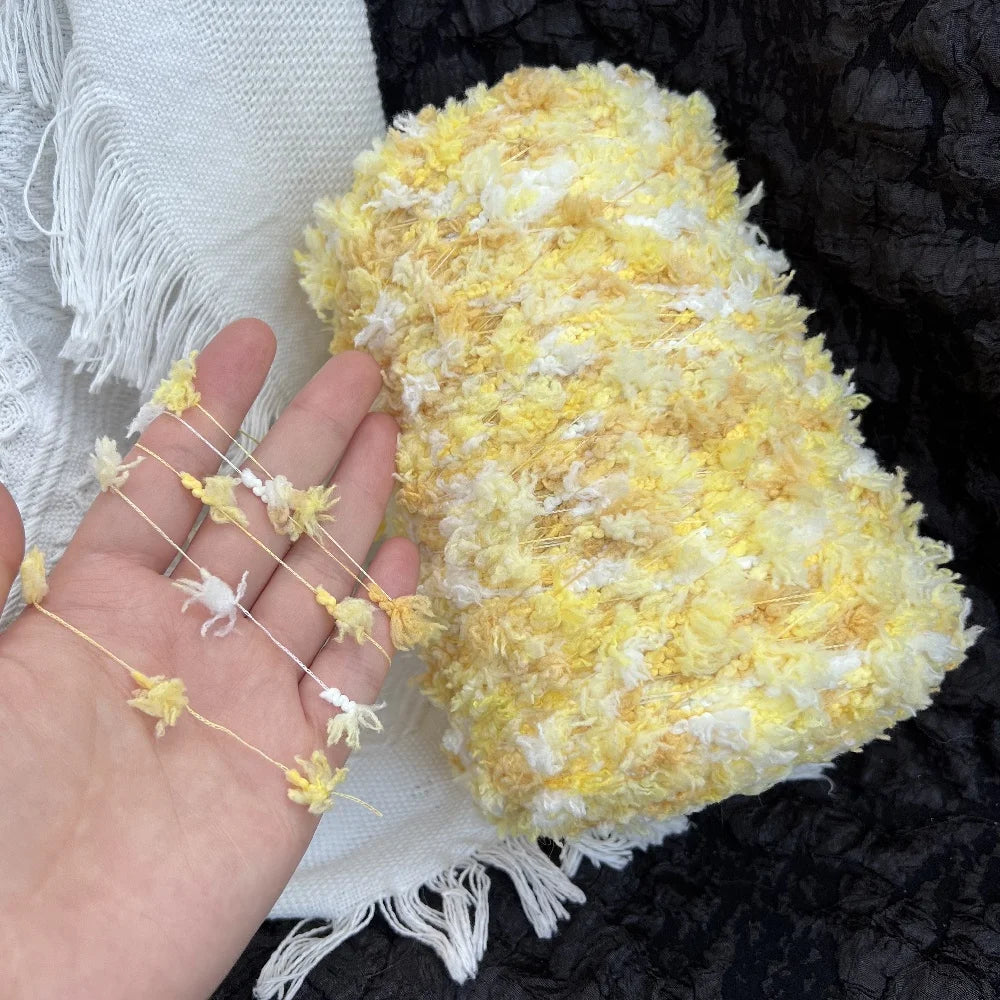A ball of hand-dyed variegated yellow and white cotton blend yarn resting on a white cloth next to knitting needles.