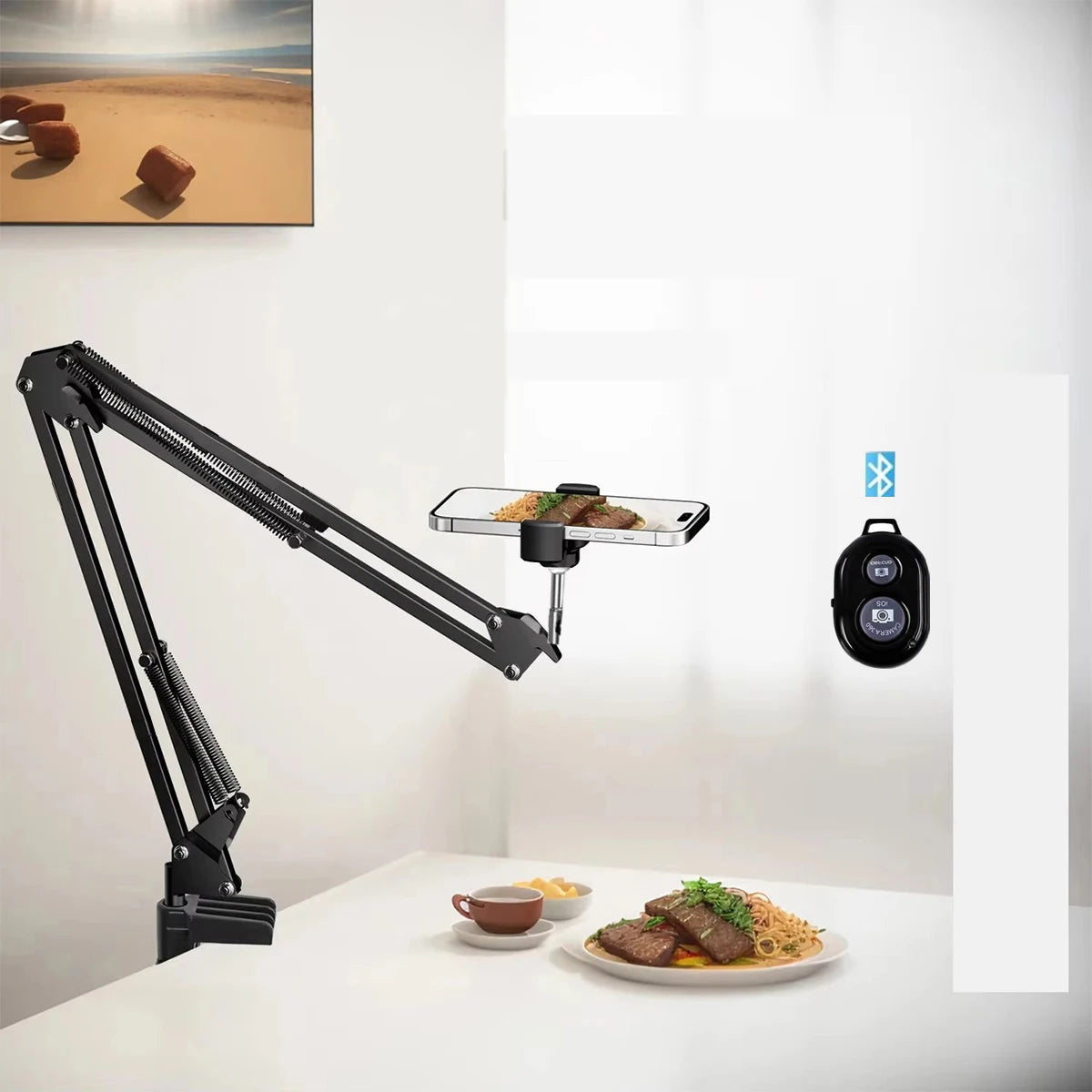 A black adjustable phone stand with overhead lighting positioned above a white table displaying food.