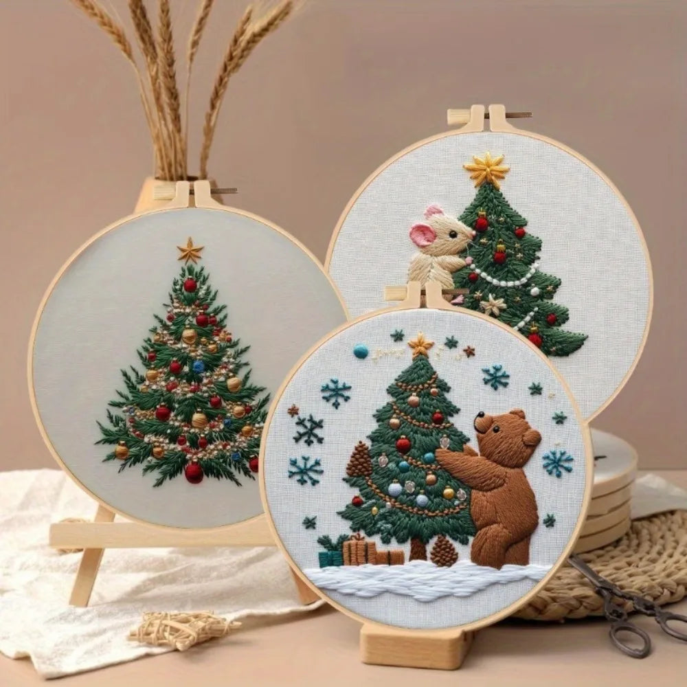 A handcrafted Christmas embroidery kit featuring a detailed green fir tree and a brown bear on a light fabric background.