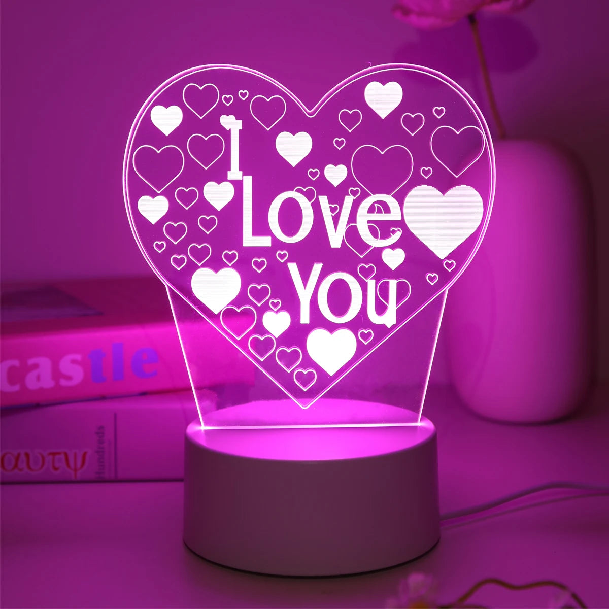 A glowing pink heart shaped LED night light with a 'I Love You' design displayed on a surface.