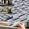 A hand is placing peel and stick waterproof tile stickers on a gray and black marble backsplash.