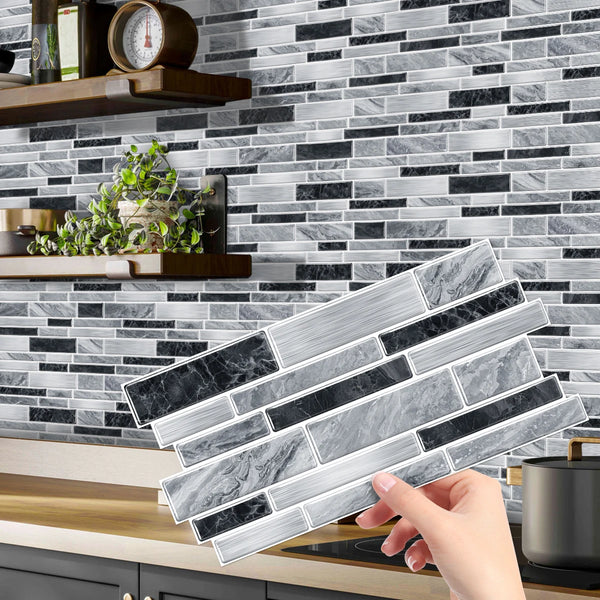 A hand is placing peel and stick waterproof tile stickers on a gray and black marble backsplash.
