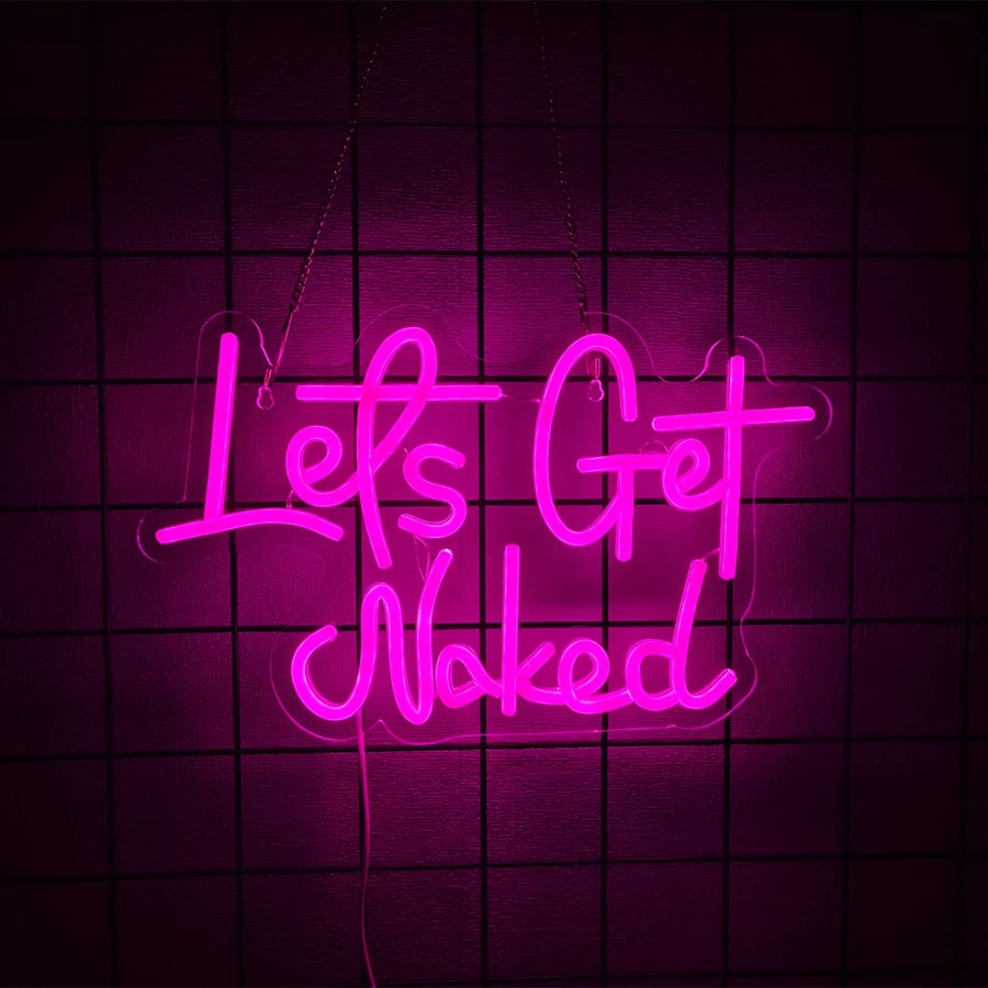 Neon sign spelling out Lets Get Naked in bright pink glowing script against a dark grid background