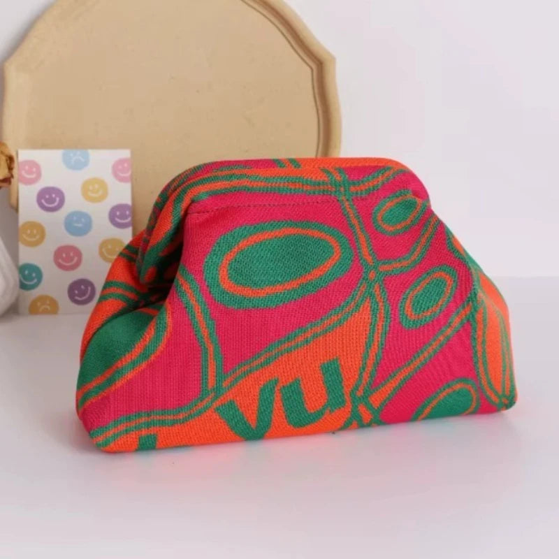A vibrant pink and orange hand-knit clutch bag with geometric patterns resting on a white surface.