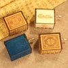 Three wooden music boxes featuring different designs and colors resting on a beige fabric.