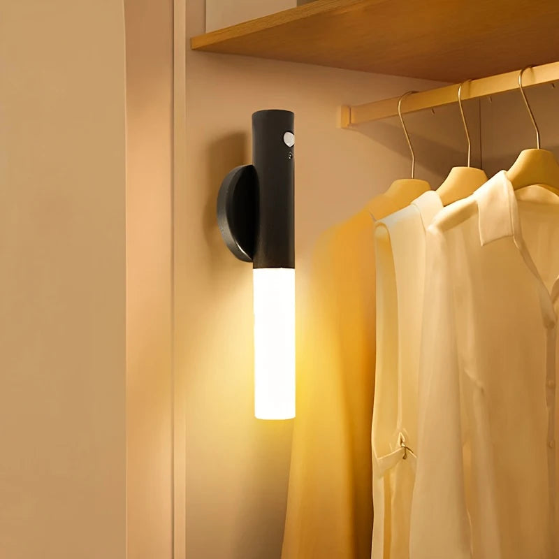 A modern magnetic LED wall light with a motion sensor mounted on a wooden shelf, illuminating a clothing rack.