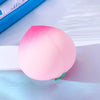Jouet anti-stress pêche rose squishy posé sur une surface bleu clair.