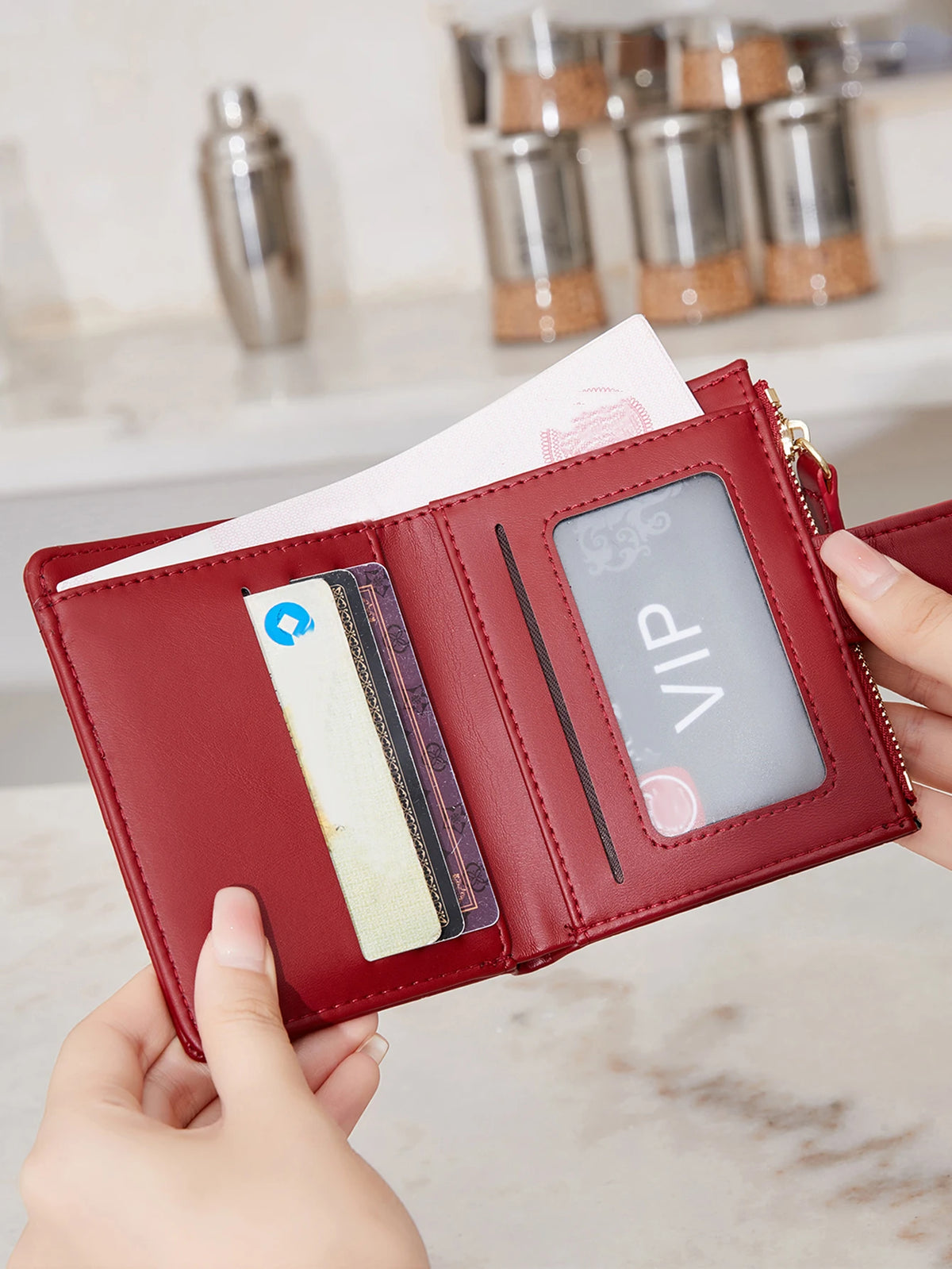 A hand holds a red leather compact zippered wallet with card slots and a VIP display.
