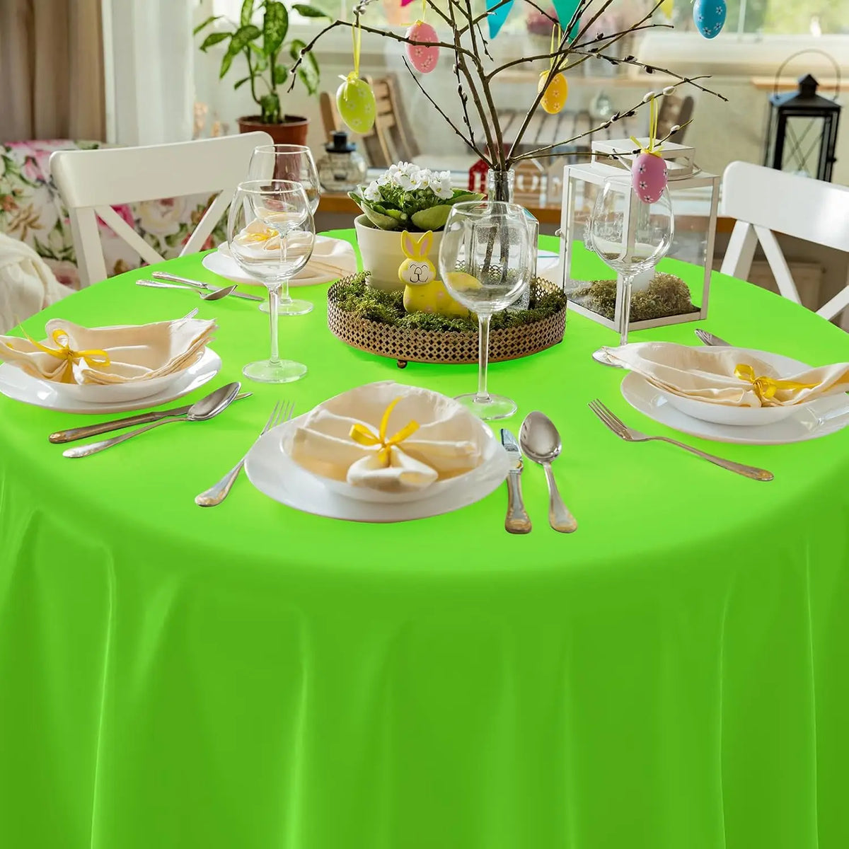 A bright green disposable round tablecloth set for parties with yellow floral accents and glassware.