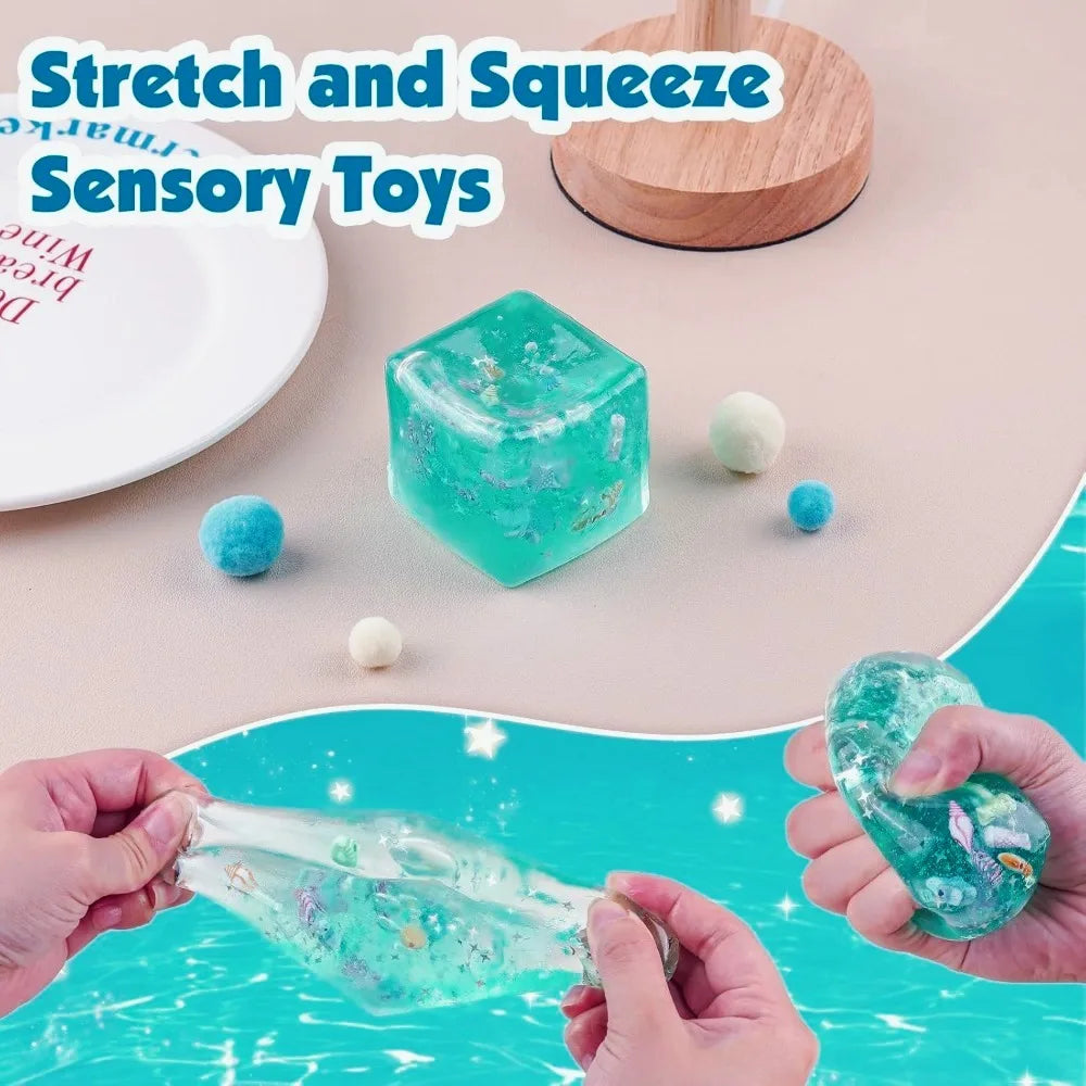 Hands squeezing a translucent teal ice cube sensory toy and a clear plastic item on a pink background.