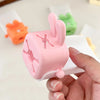 A hand holds a pink rabbit-themed anti-splash faucet extender for kids, demonstrating its design.
