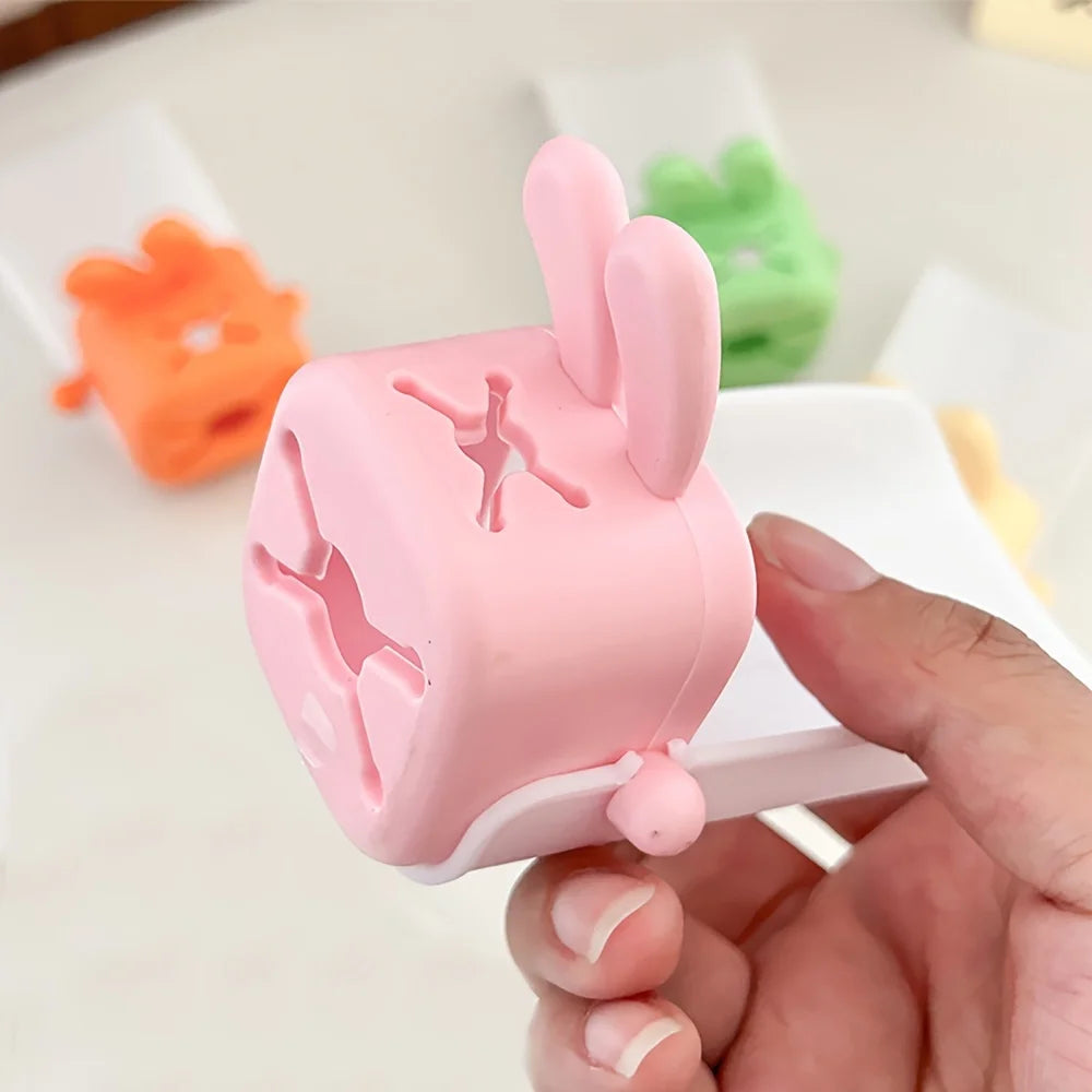 A hand holds a pink rabbit-themed anti-splash faucet extender for kids, demonstrating its design.