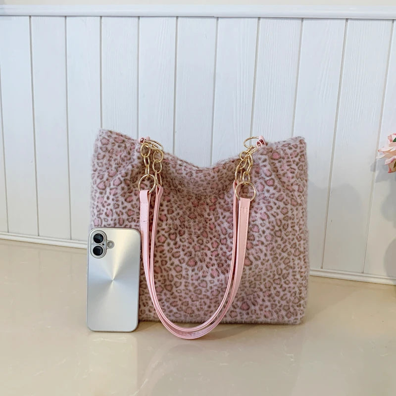 Sac en toile rose à imprimé léopard, quincaillerie dorée et sangle assortie, posé à côté d'un smartphone argenté.