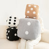 A stack of three plush pillows in various colors and polka dots resting on a light-colored sofa.