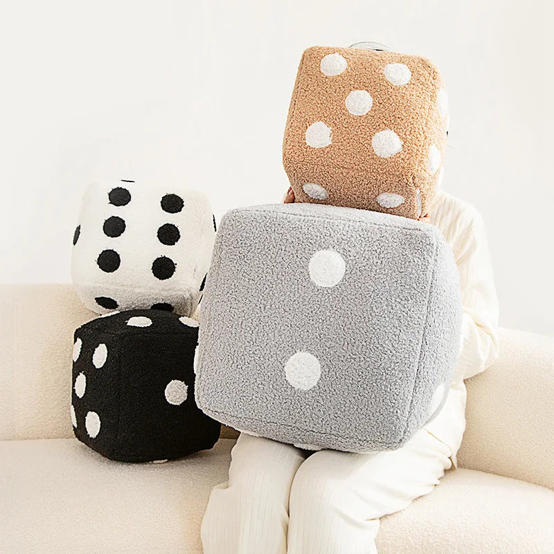 A stack of three plush pillows in various colors and polka dots resting on a light-colored sofa.