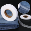 Roll of white double-sided iron-on adhesive tape next to a folded denim fabric and a circular close-up view.