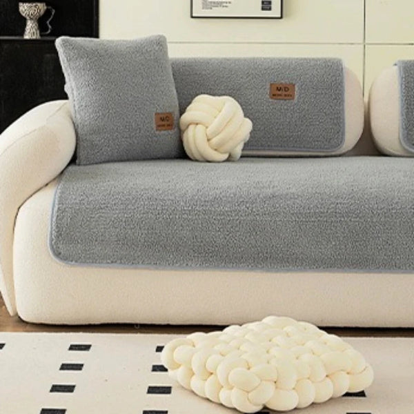 Housse de canapé sherpa gris clair avec coussins décoratifs et accent tricoté blanc sur un canapé de salon.
