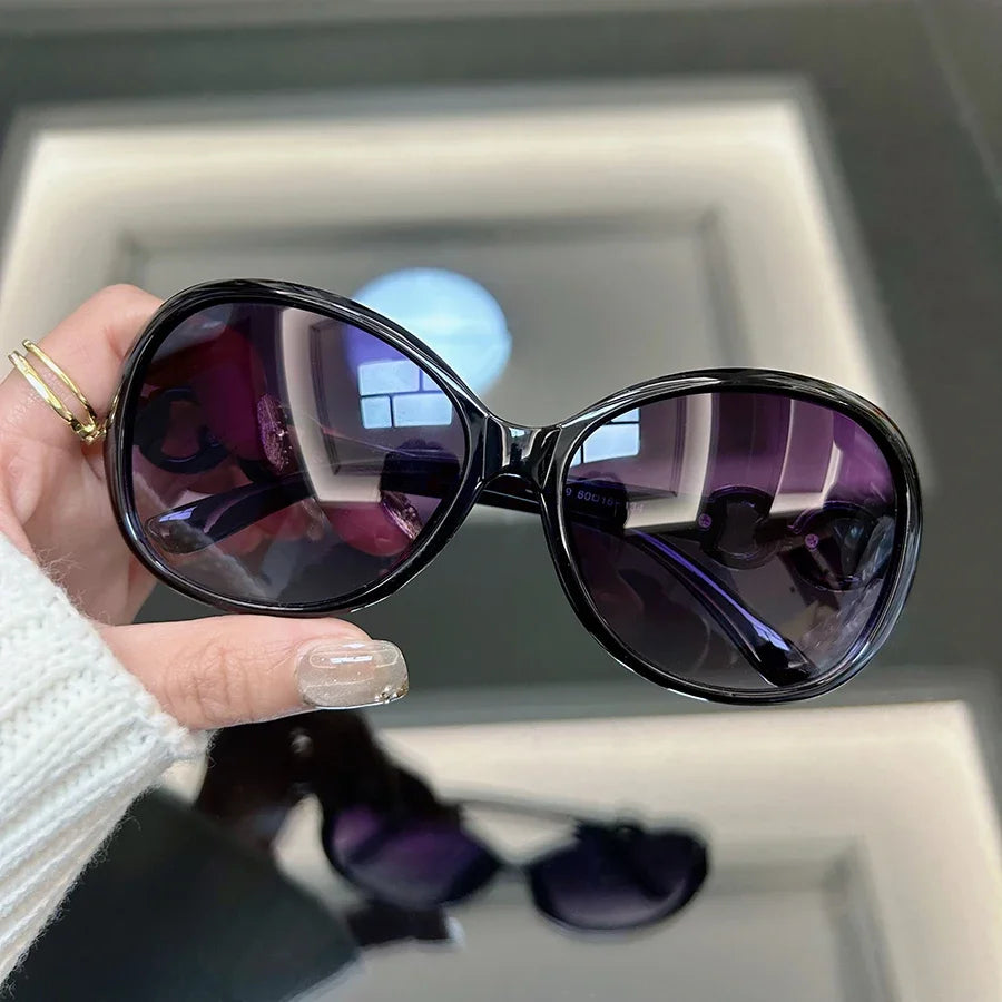 A close-up of purple vintage square sunglasses being held against a light background.