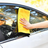 A hand is wiping a car window with a yellow microfiber cleaning towel.