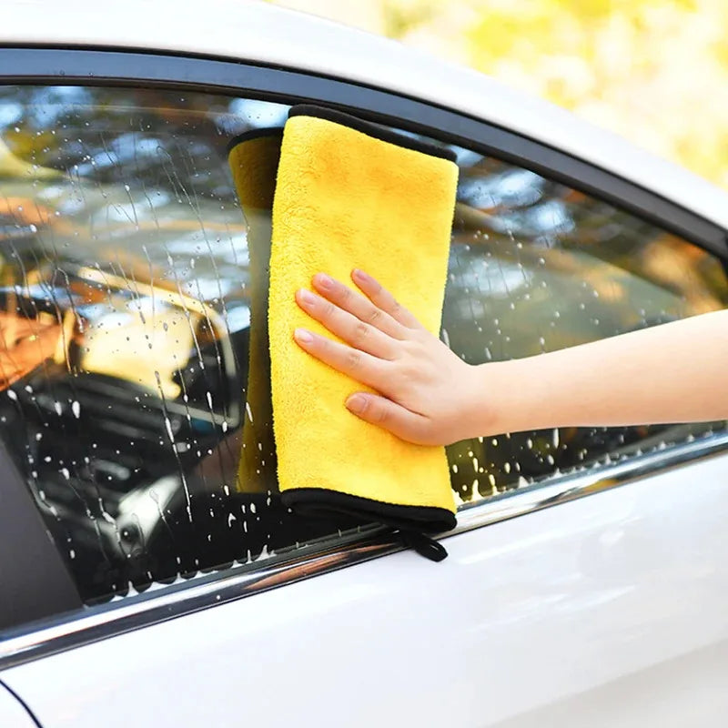 A hand is wiping a car window with a yellow microfiber cleaning towel.