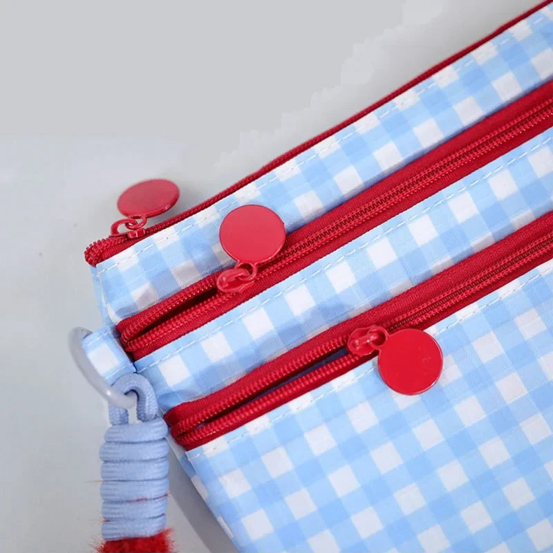 A close-up of a blue and white checkered travel passport holder with red zippers and decorative red buttons.