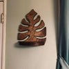 A rustic wooden wall-mounted storage rack shaped like a tropical leaf, mounted on a light-colored wall.