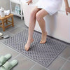 A gray anti-slip shower mat with massage points and drainage holes placed on a tiled floor.