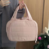 A pink quilted cosmetic travel organizer bag being held by a person against a wooden background.
