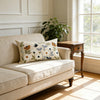 A beige sofa with a floral embroidered throw pillow on it, next to a wooden table and a large window.