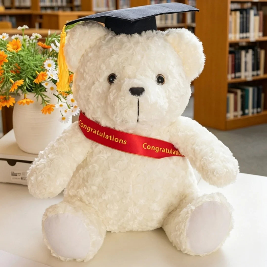 Peluche d'ours médecin de graduation blanc portant une toque noire et un ruban rouge.