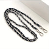 A close-up of a black and silver metal chain purse strap with a secure buckle lying on a white surface.