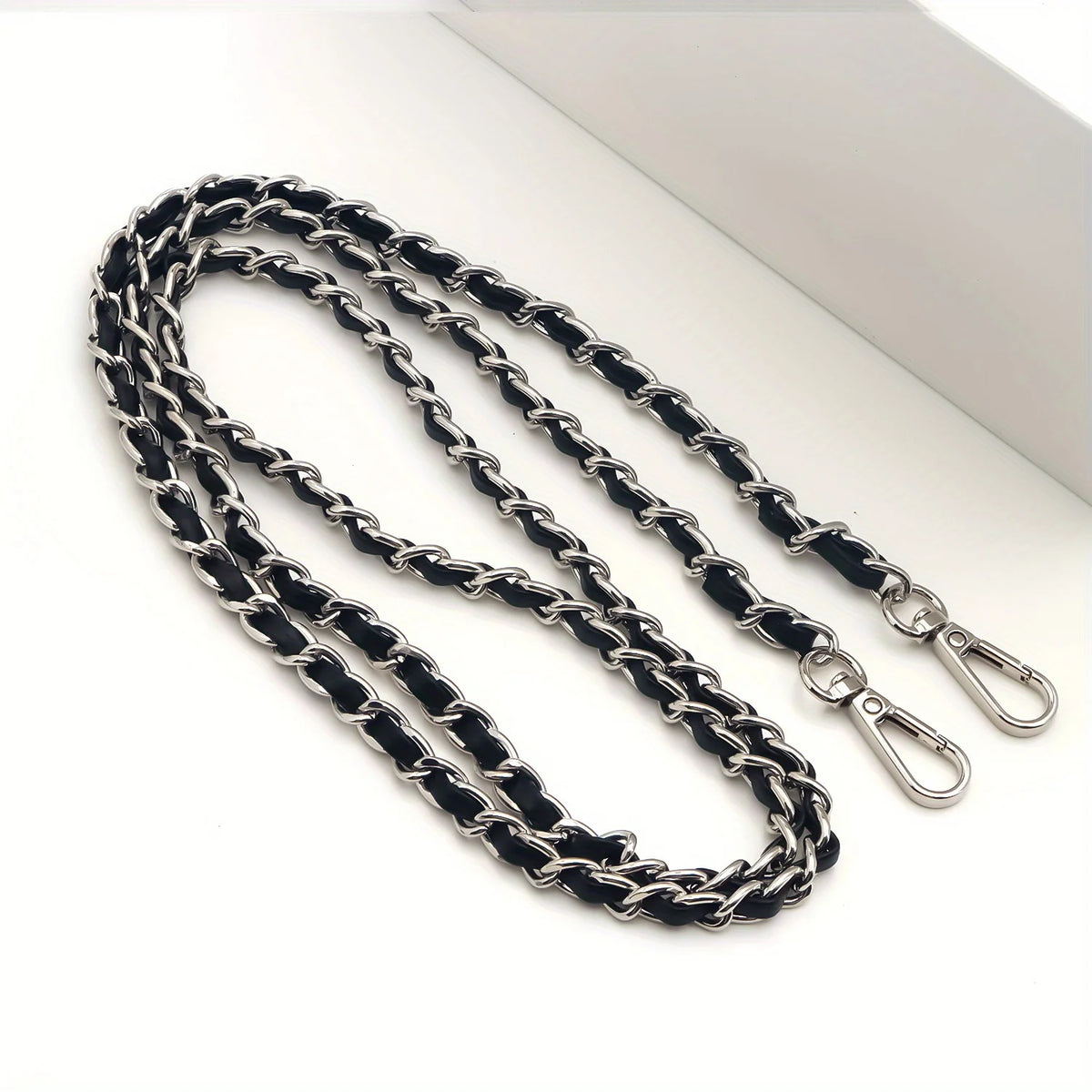 A close-up of a black and silver metal chain purse strap with a secure buckle lying on a white surface.