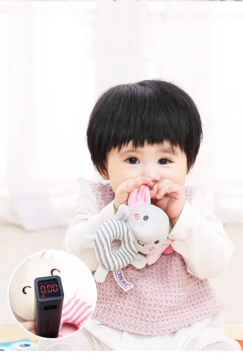 A baby is holding a soft plush rattle toy with a cartoon animal design.