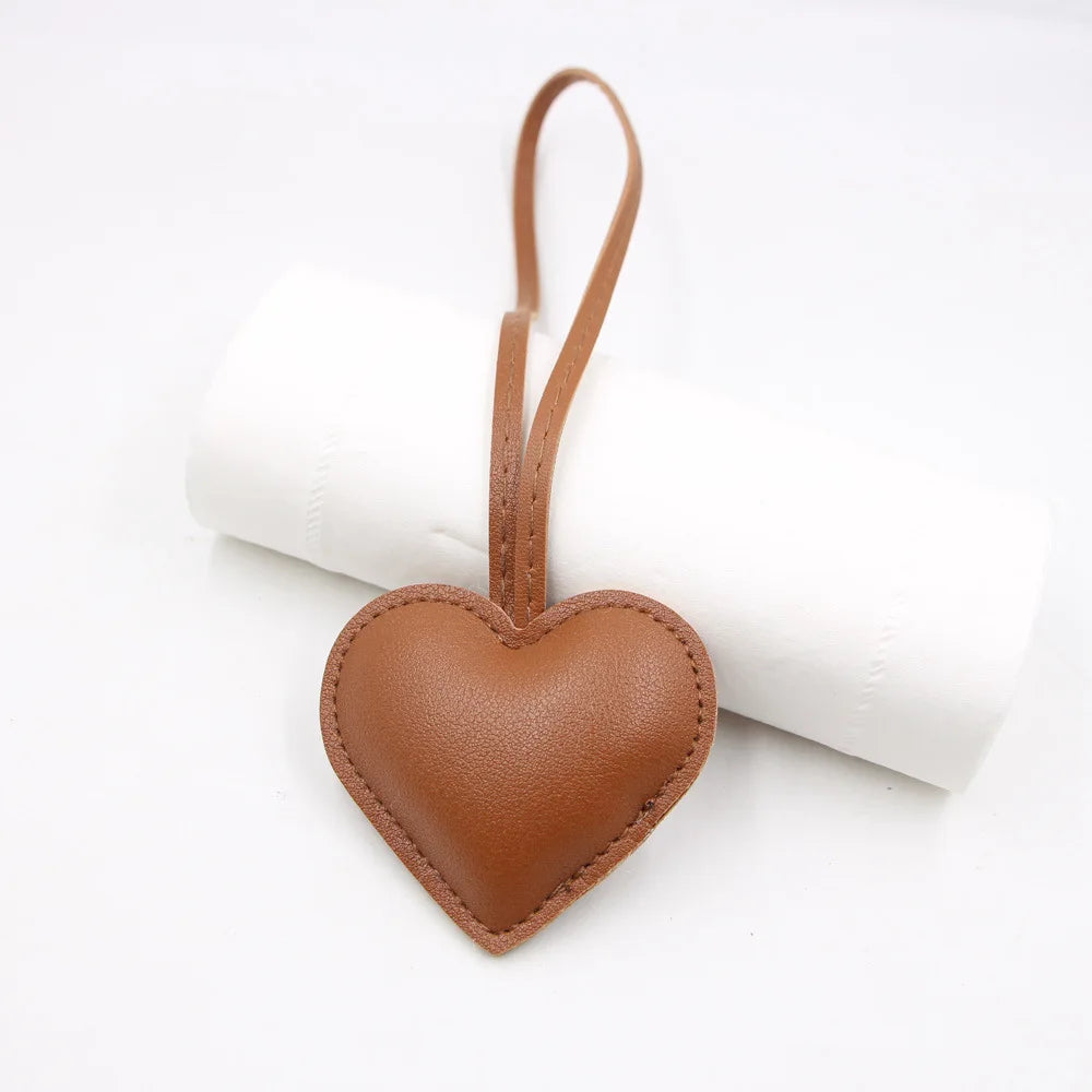 A brown heart-shaped PU leather keychain with a cotton peach charm resting on a white rolled cloth.